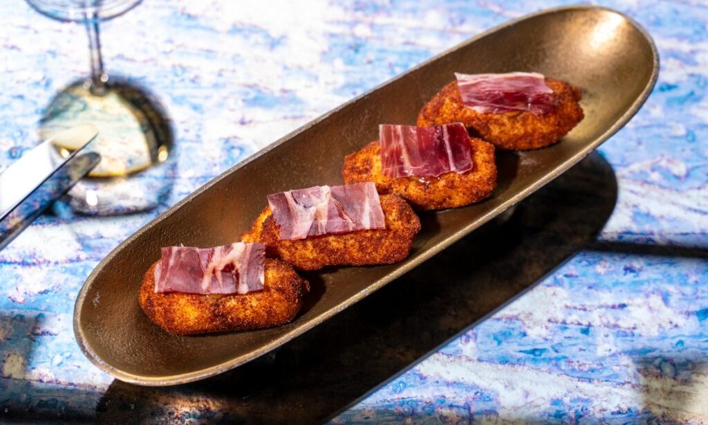 Croquetas de jamón de Papagena servidas con lonchas de jamón en bandeja dorada
